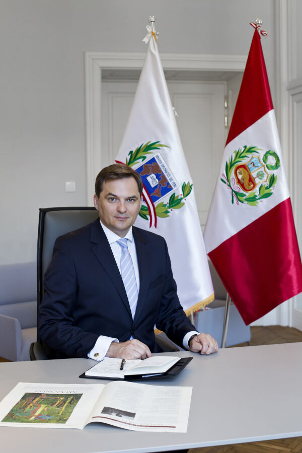 Konsul Honorowy Peru w Krakowie Marcin Mazgaj - zdjęcie portretowe Pana Mazgaja na tle flag Peru